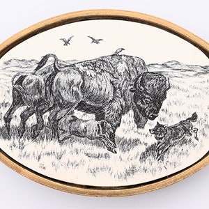 May include: A black and white illustration of a bison and a calf with birds flying overhead. The image is on a white background with a gold oval frame.