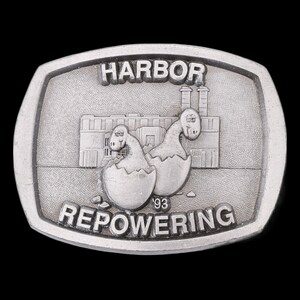May include: A silver-toned belt buckle with a cartoon image of a building with two dinosaurs hatching from eggs. The text "HARBOR REPOWERING '93" is engraved on the buckle.