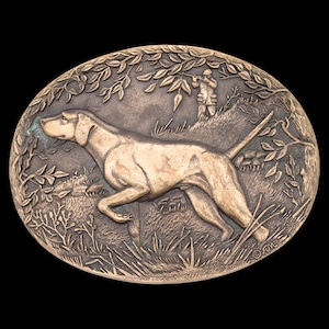May include: Oval bronze-colored relief sculpture featuring a hunting dog in a field, with a hunter in the background. The dog is in mid-stride, with detailed foliage and a textured background. The sculpture is set against a black background.