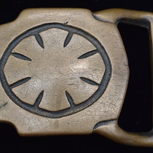 May include: A vintage brass belt buckle with a circular design featuring eight stylized petal shapes. The buckle has a rectangular shape with a loop for the belt strap.