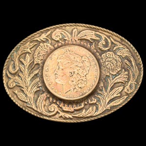 May include: Oval-shaped, antique gold-toned belt buckle featuring a central coin with a profile portrait. The buckle is adorned with floral and foliate relief patterns around the coin and along the outer edge, creating a vintage aesthetic.