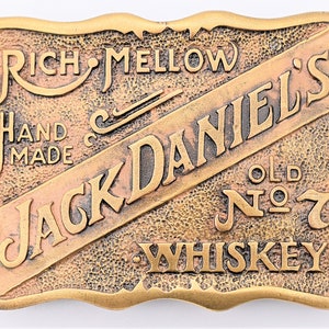 May include: A gold-colored metal belt buckle with the words "Jack Daniel's" in a diagonal script across the front. The buckle also features the words "Rich Mellow", "Hand Made", "Old No. 7", and "Whiskey".