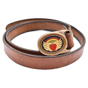 May include: A brown leather belt with a gold-colored buckle. The buckle features a heart with wings, a rainbow, and a blue border. The belt is approximately 1 inch wide.