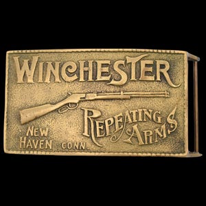 May include: A rectangular brass belt buckle featuring the Winchester Repeating Arms logo. The design includes the Winchester name, a rifle illustration, and the text "Repeating Arms" and "New Haven Conn."