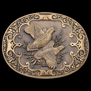 May include: Oval-shaped, bronze-toned belt buckle featuring two detailed birds in flight, set against a textured background. The buckle is framed by an ornate, scrolling border with floral and leaf accents. The birds are the focal point, with intricate feather detailing.