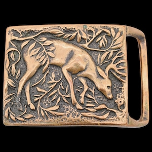 May include: A rectangular bronze-colored belt buckle featuring a detailed relief of a deer grazing amidst foliage. The deer is depicted with antlers, surrounded by leaves and branches, with a classic buckle design.