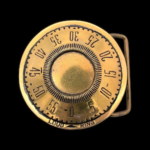 May include: A vintage brass belt buckle with a circular design resembling a dial. The numbers 0-55 are displayed around the edge. The words "LOUD" and "RING" are at the bottom.