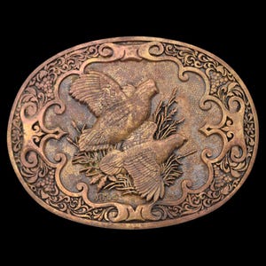 May include: Oval-shaped, bronze-colored belt buckle featuring two birds in flight, set against a backdrop of wheat and ornate scrollwork. The buckle has a detailed, embossed design with a vintage aesthetic.