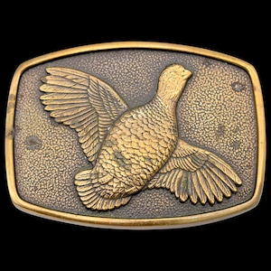 May include: A rectangular, vintage-style belt buckle with a detailed relief of a bird in flight. The bird and the buckle's frame are gold-toned, set against a textured, dark background. The buckle is likely made of metal.
