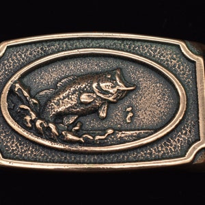 May include: A bronze belt buckle with a detailed design of a bass fish jumping out of the water.