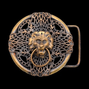 May include: Ornate, antique-style belt buckle with a lion's head centerpiece. The buckle features a circular design with intricate filigree and a bronze finish. The lion's head has a ring in its mouth.