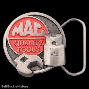 May include: A round silver-toned metal belt buckle featuring a red circular inlay with the embossed silver text MAC QUALITY TOOLS. The design includes a raised silver wrench and a socket tool with the word MAC engraved on the side of the socket.
