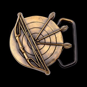 May include: Vintage brass belt buckle featuring a target with arrows, a bow, and the text "©1979 BTS". The buckle has a rectangular frame and a detailed design, perfect for archers or those who appreciate vintage accessories.