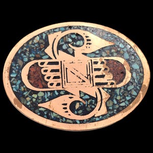 May include: Oval-shaped copper-colored pendant with a mosaic design. The mosaic features turquoise and red stone fragments. A copper-colored design is overlaid on the mosaic, featuring a central rectangular shape and curved elements on either side.
