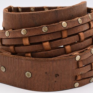 May include: A brown leather belt with a woven design and silver studs. The belt is rolled up and the woven design is visible.