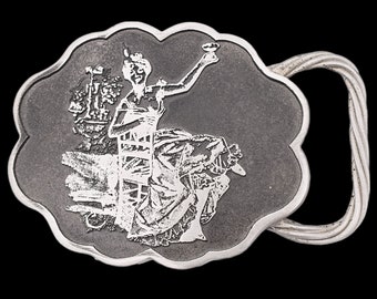 May include: Silver-toned belt buckle with a detailed relief of a woman seated in a chair, raising a cup. A ship is depicted to her left. The buckle has a decorative, scalloped edge and a twisted metal loop.