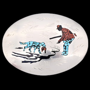 May include: A silver belt buckle with an inlaid design of a hunter with two dogs. The hunter is wearing a red and blue outfit and is holding a rifle. The dogs are brown and white and are running through a field.