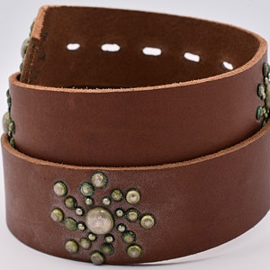 May include: A brown leather belt with silver and green metal embellishments. The belt is folded in half and the embellishments are visible on both sides.