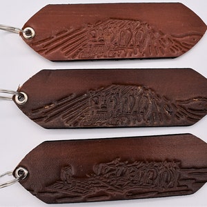 May include: Three brown leather keychains with silver key rings. Each keychain has a different design embossed on the leather. The designs are all similar, but each has a slightly different angle.