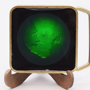 May include: A brass belt buckle with a green glass globe inset. The globe has a raised, textured design of the continents.