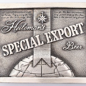May include: A silver belt buckle with a raised image of a globe, a ribbon, and the text "Heileman's Special Export Beer".