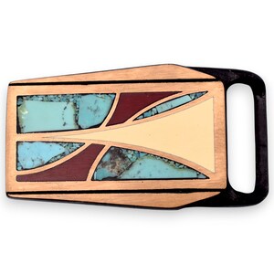 May include: A rectangular belt buckle with a copper-colored frame and a black loop. The buckle features turquoise-colored stone inlays, dark red accents, and a cream-colored central design. The overall design is geometric.