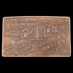 May include: A bronze-colored metal plaque with an illustration of a space launch complex. The text "FIRST MANNED POLAR ORBIT SPACE LAUNCH COMPLEX 6 VAFB" is engraved on the plaque.