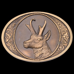 May include: Oval-shaped, bronze-colored belt buckle featuring a detailed relief of a deer's head with antlers. The deer is centered within a circular frame, surrounded by floral and scrollwork designs. The buckle has a gold-colored border.