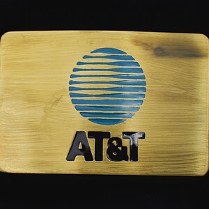 May include: A gold-colored metal belt buckle with a blue and white globe design and the text "AT&T" in black.