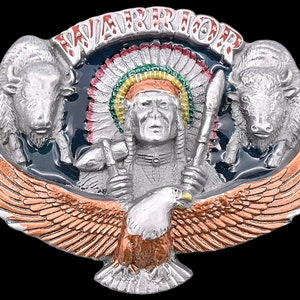 May include: A silver-toned metal belt buckle with a Native American chief design. The buckle features a central figure of a chief with a headdress, flanked by two bison and an eagle. The word "WARRIOR" is arched across the top.