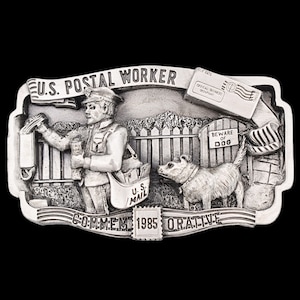 May include: A silver belt buckle with a three-dimensional design of a mail carrier delivering mail to a house with a dog. The buckle has the text "U.S. POSTAL WORKER" and "COMMEME 1985 ORATIVE".