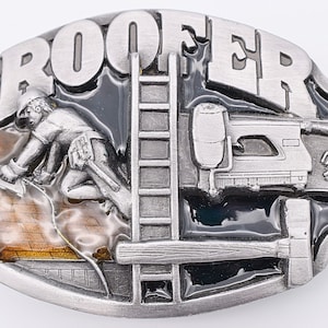 May include: Silver-toned metal belt buckle with a detailed relief design. The word "ROOFER" is at the top. The design includes a roofer, a ladder, a nail gun, and a hammer. The background is black enamel.