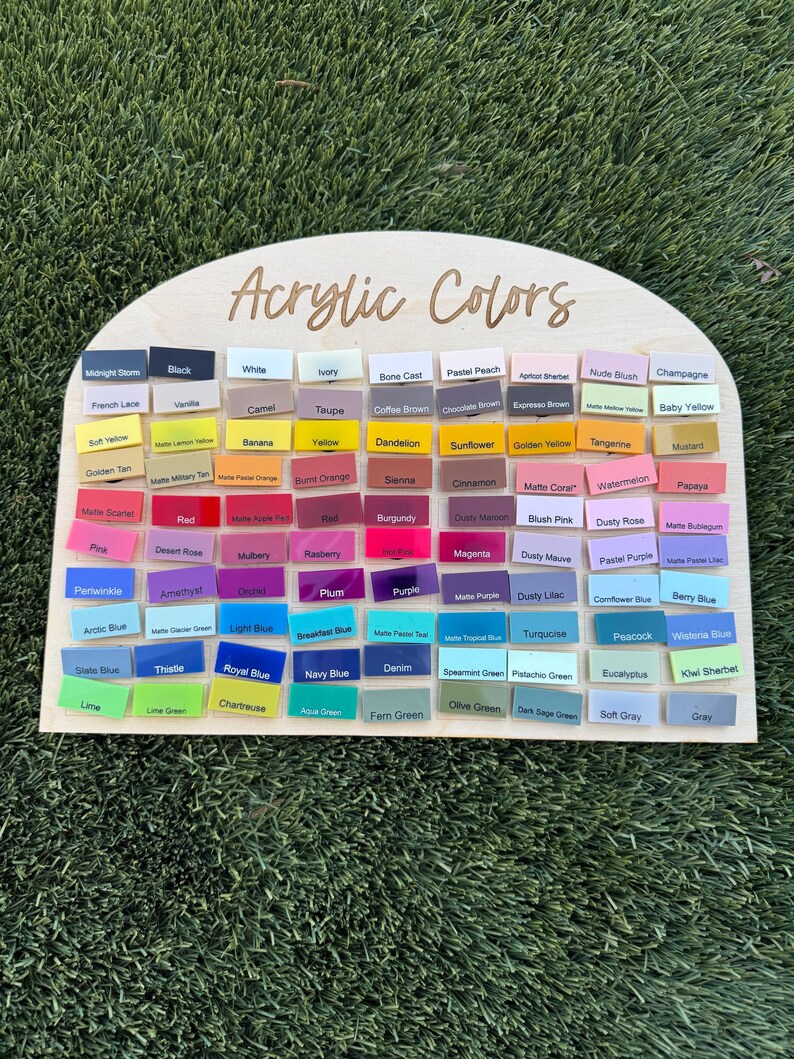 May include: A semi-circular wooden display board with the text Acrylic Colors printed at the top. It features a grid of numerous small rectangular acrylic swatches in a wide variety of colors, each labeled with its specific color name in black text.