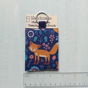 May include: A rectangular fabric pouch featuring a navy blue background with a repeating orange fox and floral pattern. The pouch has a dark blue fabric loop attached to a silver metal keyring. A tag reads 5 Handmade Glass Cleaning Pouch.