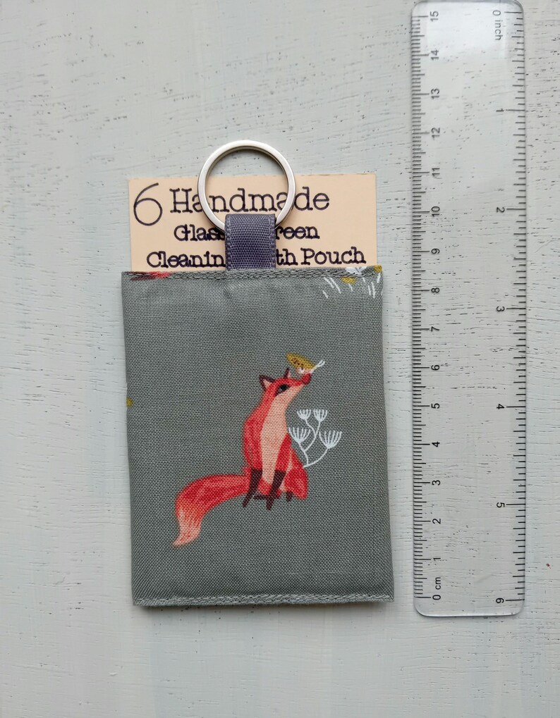 May include: A gray fabric pouch featuring a red fox illustration, a purple fabric loop, and a silver metal keyring. The pouch is attached to a beige card labeled 6 Handmade Glass Screen Cleaning Pouch. A clear ruler shows the pouch is 4 inches tall.