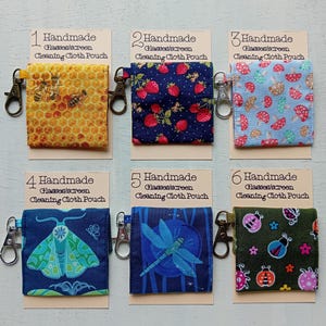 May include: Six square fabric pouches for cleaning glasses or screens, each attached to a metal lobster clasp. Designs include bees on honeycomb, strawberries, mushrooms, a moth, a dragonfly, and ladybugs, all labelled with numbered cards.