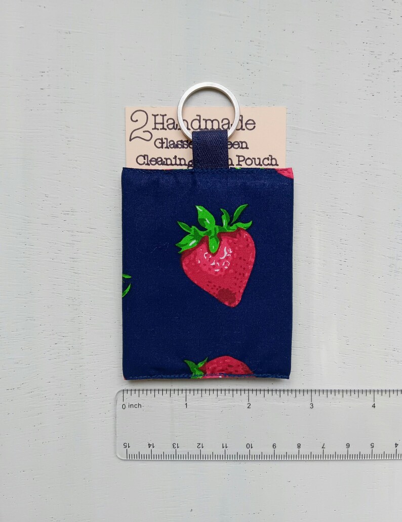 May include: A navy blue fabric pouch with a strawberry print, featuring a silver metal keyring. A tag reads 2 Handmade Glasses Cleaning Pouch. A clear ruler shows the pouch is approximately 3 inches wide and 4 inches tall.