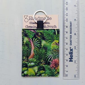 May include: A rectangular fabric pouch featuring a green dinosaur and fern print, attached to a silver metal keyring. A beige card behind the pouch reads "Handmade Glass Cleaning Cloth Pouch". A ruler shows the pouch is approximately 3.5 inches tall.
