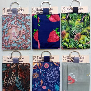 May include: Six rectangular fabric pouches with metal key rings, each attached to a card labeled 1 through 6. The pouches feature various prints including a sleeping animal, strawberries, dinosaurs, floral patterns, a fox, and a small animal on sage green.