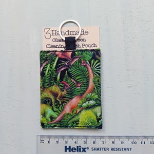 May include: A rectangular fabric pouch featuring a colorful dinosaur and fern print, attached to a silver metal keyring. The pouch is displayed with a card labeled 3 Handmade Glasses Cleaning Cloth Pouch and a ruler measuring approximately 3.5 inches.