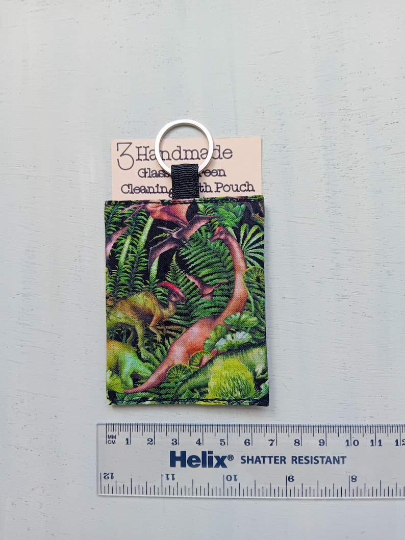May include: A rectangular fabric pouch featuring a colorful dinosaur and fern print, attached to a silver metal keyring. The pouch is displayed with a card labeled 3 Handmade Glasses Cleaning Cloth Pouch and a ruler measuring approximately 3.5 inches.