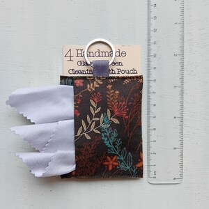 May include: A dark brown fabric pouch with a floral pattern containing white cleaning cloths, attached to a metal keyring. A clear plastic ruler shows the pouch is approximately 3.5 inches wide. The label reads 4 Handmade Glass Cleaning Cloth Pouch.