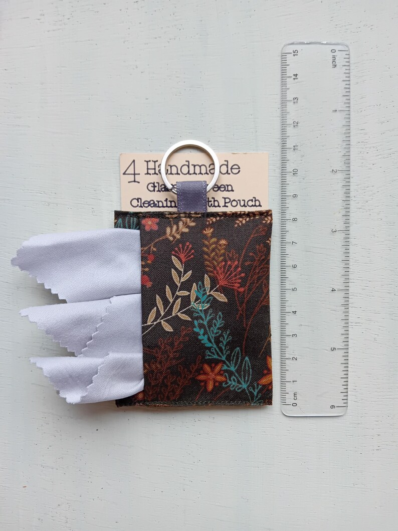 May include: A dark brown fabric pouch with a floral pattern containing white cleaning cloths, attached to a metal keyring. A clear plastic ruler shows the pouch is approximately 3.5 inches wide. The label reads 4 Handmade Glass Cleaning Cloth Pouch.