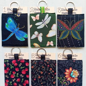 May include: Six fabric keyrings with various patterns. Designs include a blue dragonfly, butterflies, strawberries, and floral motifs. Each keyring has a metal ring and a tag that reads "Handmade Glassreen."
