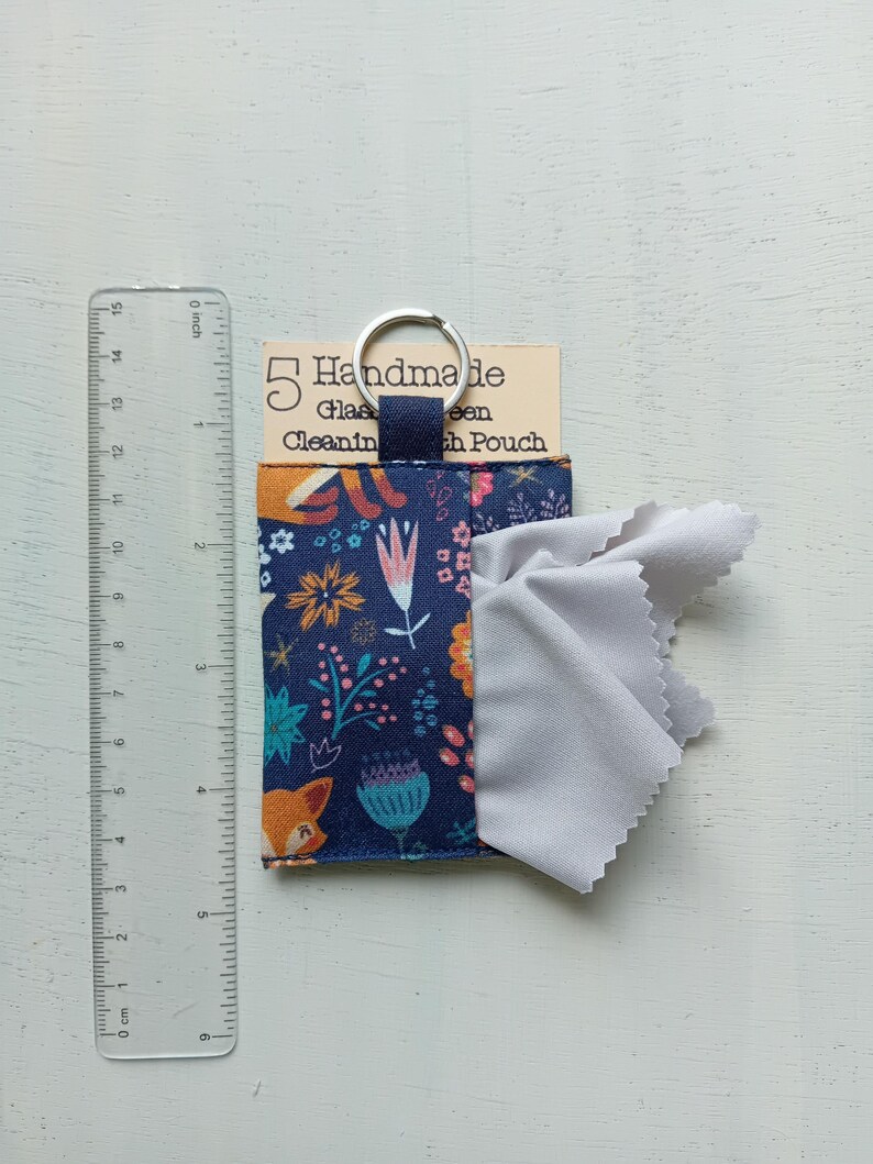 May include: A navy blue fabric pouch with a colorful floral and fox pattern, featuring a silver keyring and a light gray cleaning cloth. A clear plastic ruler shows the pouch is approximately 3.5 inches wide and 3.5 inches tall.