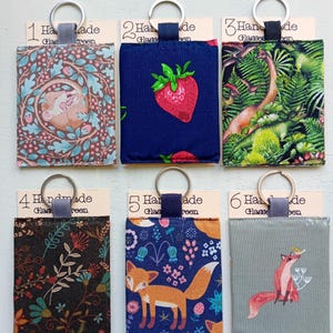 May include: Six rectangular fabric pouches with metal key rings, each attached to a numbered card labeled Handmade Glasses Screen. Designs include a mouse in foliage, strawberries on navy, a dinosaur forest, dark floral, foxes on blue, and a fox on gray.
