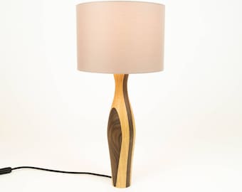 May include: A wooden table lamp with a light brown and dark brown patterned base and a light pink lampshade.