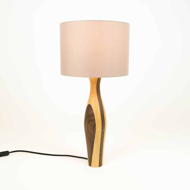 May include: A wooden table lamp with a light brown and dark brown patterned base and a light pink lampshade.