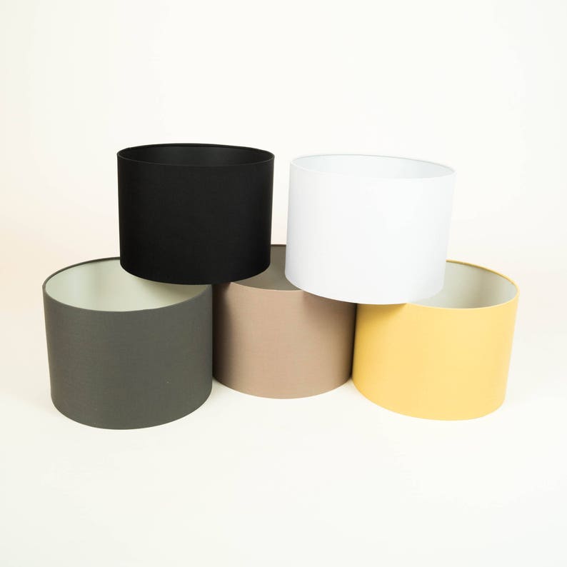 May include: Five lampshades in different colors: black, white, gray, beige, and yellow. The lampshades are all cylindrical and made of fabric.