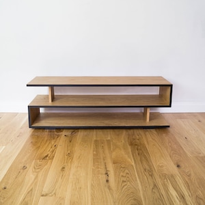 May include: A two-tiered wooden shelf unit with a black trim. The shelf is made of light wood and has a simple, modern design.